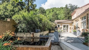 A courtyard with a small pond, surrounded by dense greenery and a building with a tiled roof. - La Magnanerie (Aubignosc)