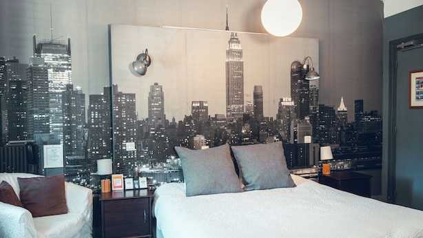 A hotel room with a cityscape view, a bed, a nightstand, a lamp, and a chair. - La Magnanerie (Aubignosc)