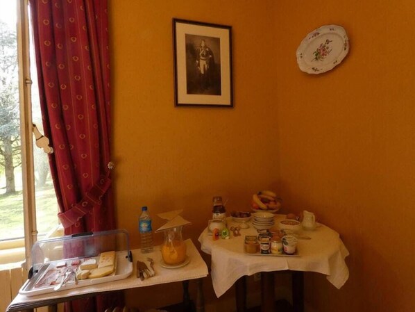 A breakfast setup with a table, a window with red curtains, a framed picture, and a plate on the wall. - Domaine de Chatenay (Saint-Saturnin)
