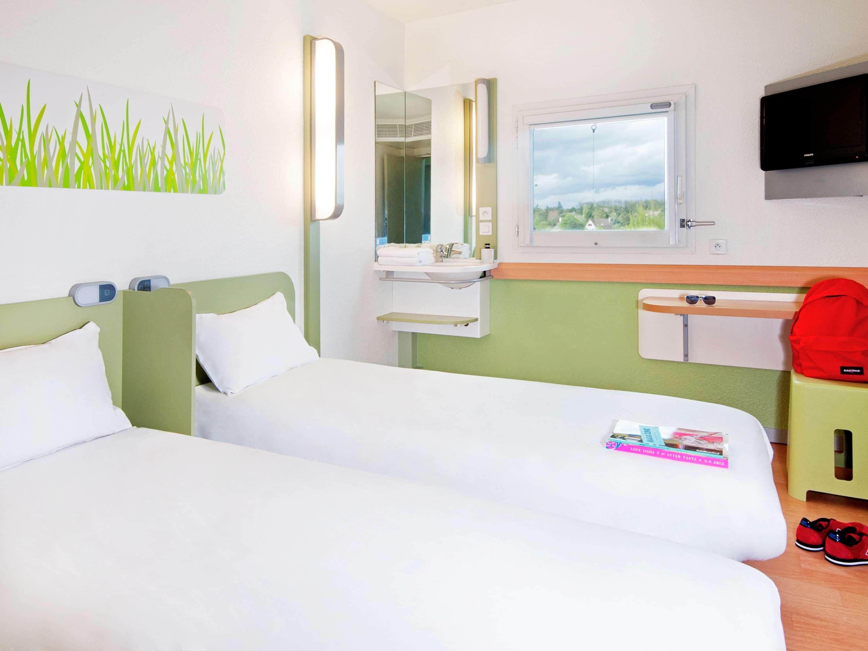 Habitación de hotel con dos camas, un baño con espejo, una ventana y un televisor.