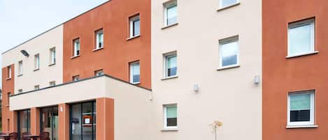 Un edificio moderno con techo plano, varias ventanas y un pequeño espacio al aire libre con sillas.