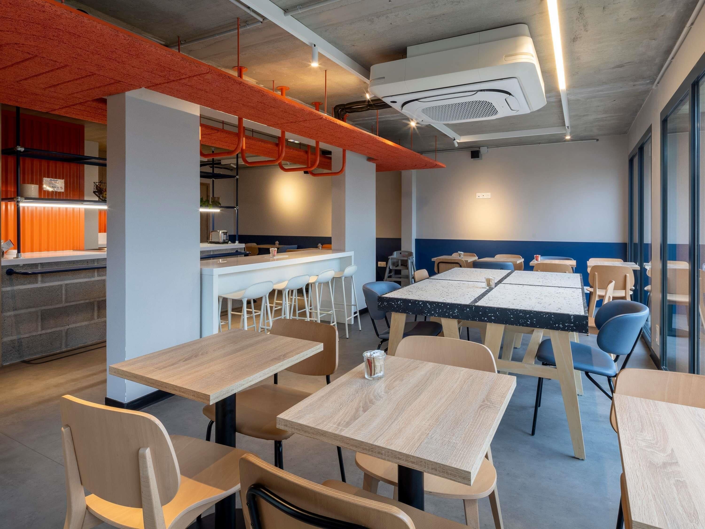 A modern dining area with tables and chairs, a bar area, and a kitchen in the background.