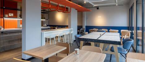 A modern dining area with tables and chairs, a bar area, and a kitchen in the background.