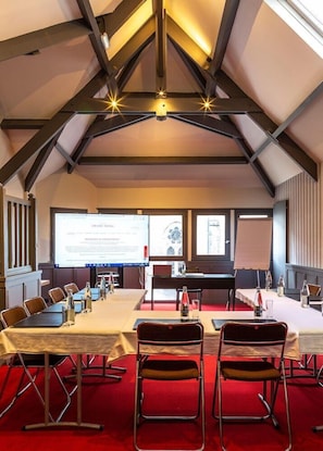 A conference room with a high ceiling, exposed beams, and a large screen for presentations. Tables and chairs are arranged for meetings. - Grand Hotel Benodet Abbatiale (Benodet)