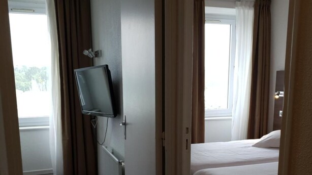 A hotel room with a bed, a television mounted on the wall, and a window with curtains. - Grand Hotel Benodet Abbatiale (Benodet)