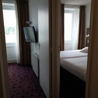 Une chambre d’hôtel avec un lit, un téléviseur fixé au mur et une fenêtre avec des rideaux.