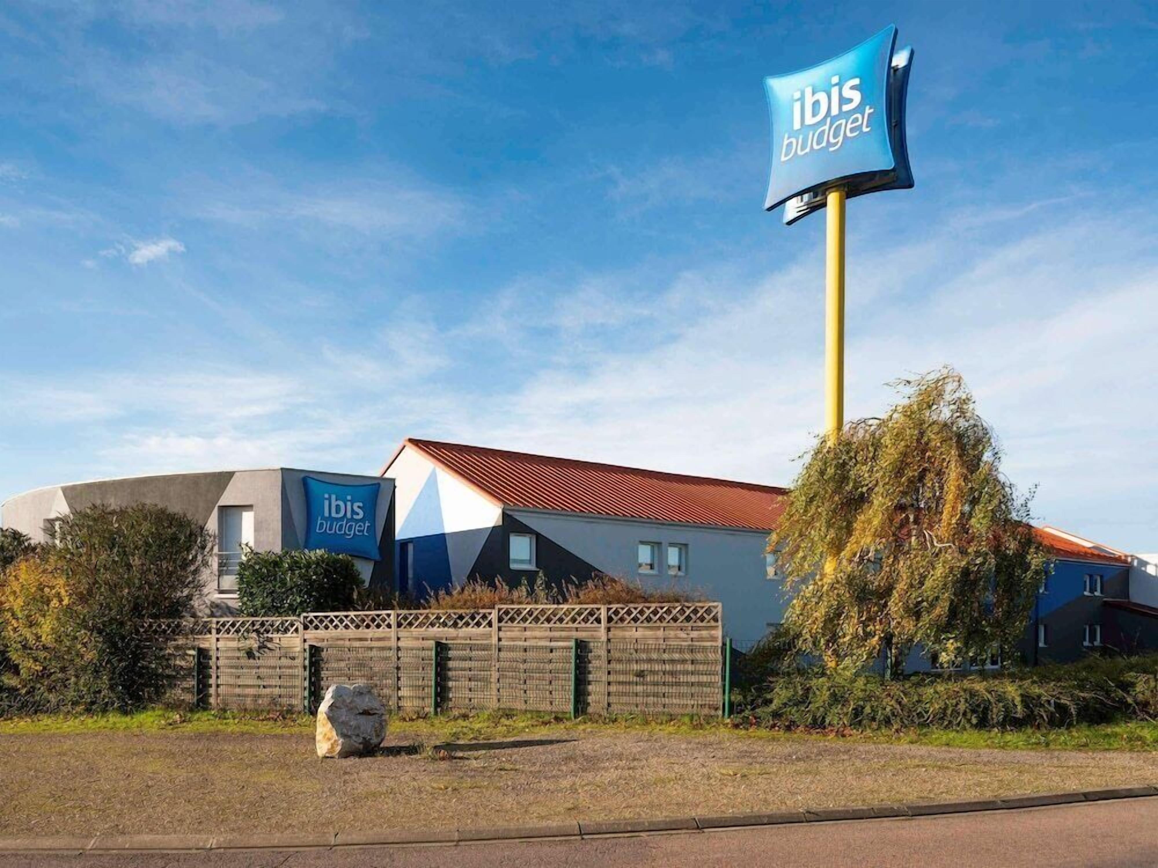 En modern byggnad med en böjd fasad, en tydlig skylt med texten ”ibis budget”, och ett rött tak.