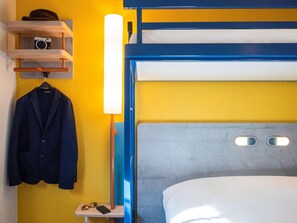A bunk bed with a grey headboard, a shelf with a camera and a hat, and a small table with a jacket and a smartphone. - Ibis Budget Nuits-saint-georges (Nuits-Saint-Georges)