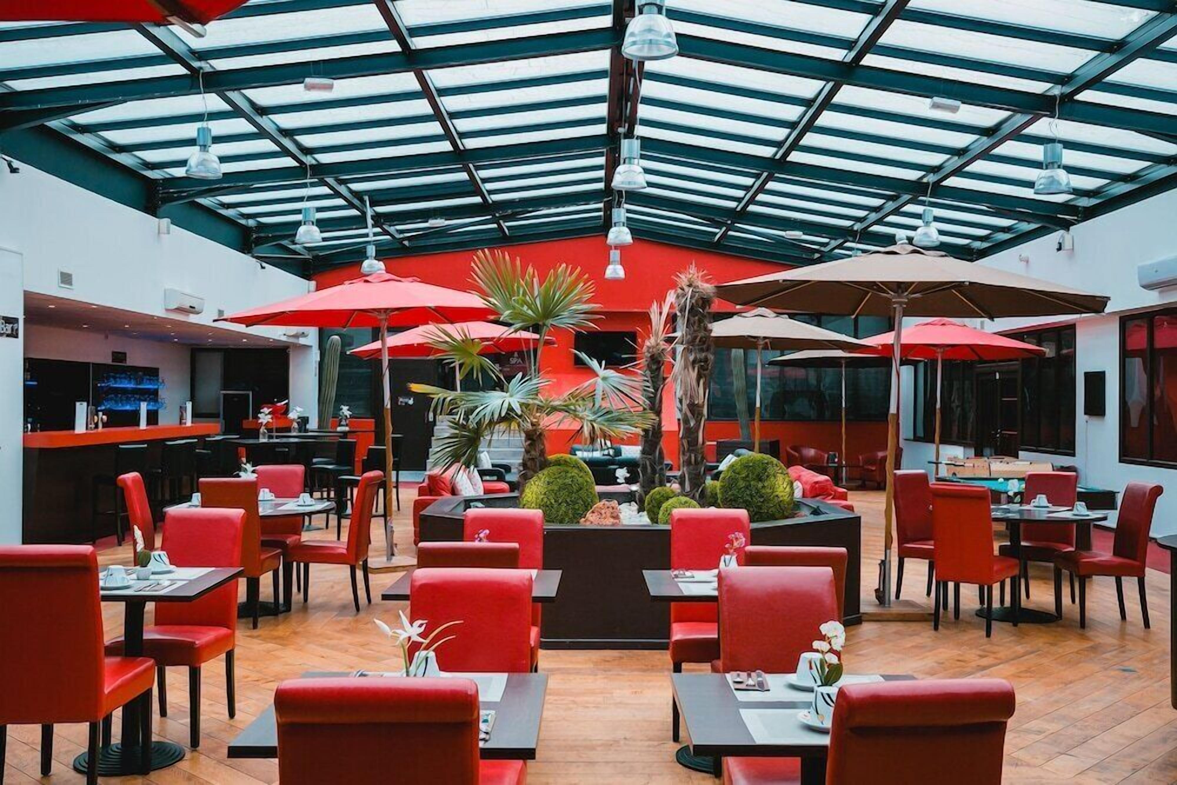 Un restaurant avec des chaises et des tables rouges, un plafond en verre et des plantes en pot.