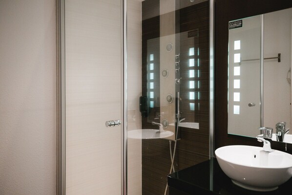 A modern bathroom with a glass shower enclosure, a white sink, and a large mirror. - Zenia Hotel And Spa (Proville)