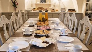 Ein langer Esstisch ist für ein Frühstück gedeckt, mit weißen Stühlen, einer Kristallleuchtreiter und einer weißen, gewölbten Decke.