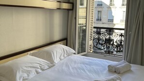 A hotel room with a bed, two pillows, a window with curtains, and a view of a building. - Hotel De France (Bordeaux)