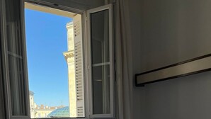 A hotel room with two beds, a window with blinds, a magazine on the bed, and a nightstand. - Hotel De France (Bordeaux)