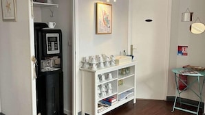 A room with a microwave, a white cabinet with shelves, a clock, and a framed picture on the wall. - Hotel De France (Bordeaux)