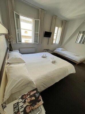 A hotel room with two beds, a flat-screen TV, a window with curtains, and a magazine on the floor. - Hotel De France (Bordeaux)