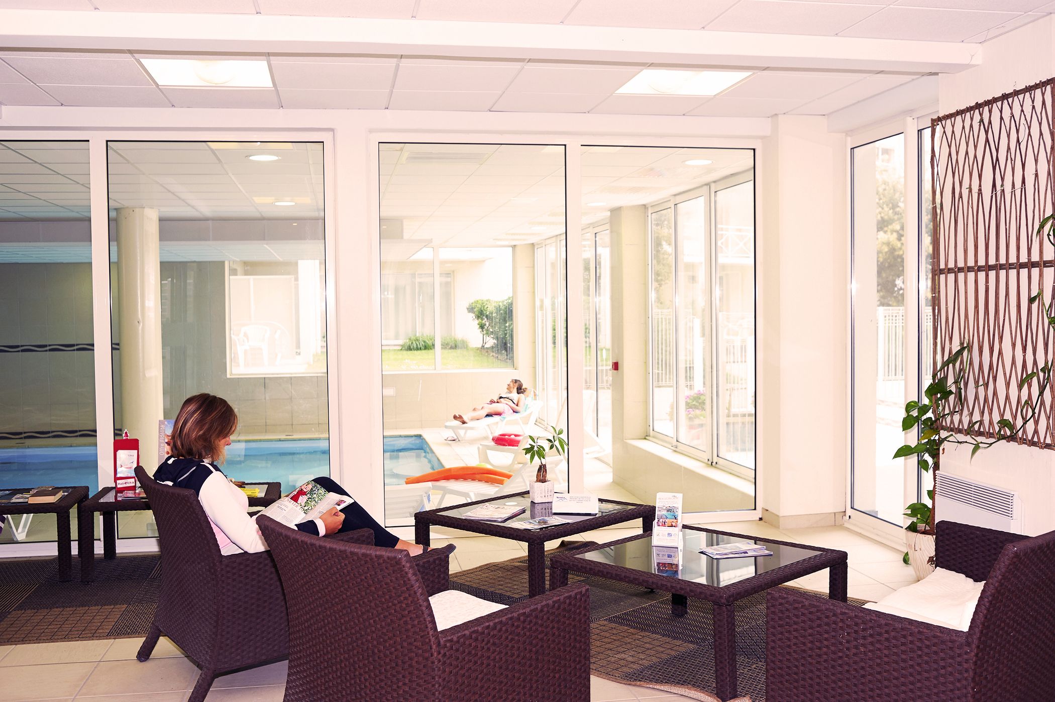 A hotel lobby with wicker furniture, a glass coffee table, and a view of an outdoor pool area.