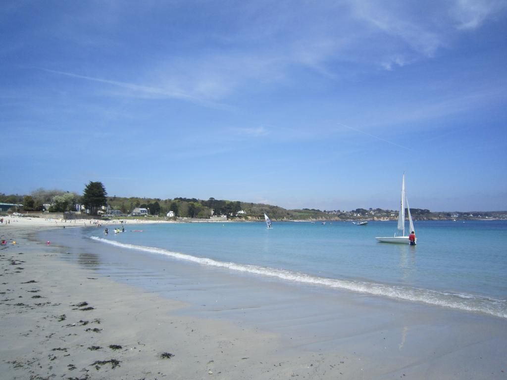 A beach with clear water, a sailboat, and a distant shoreline with buildings.