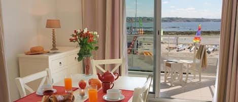 Un coin repas avec une table mise pour le petit-déjeuner, une vue sur la plage et un balcon donnant sur la mer.