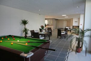 A pool table with balls, a dining area with chairs and tables, and potted plants.