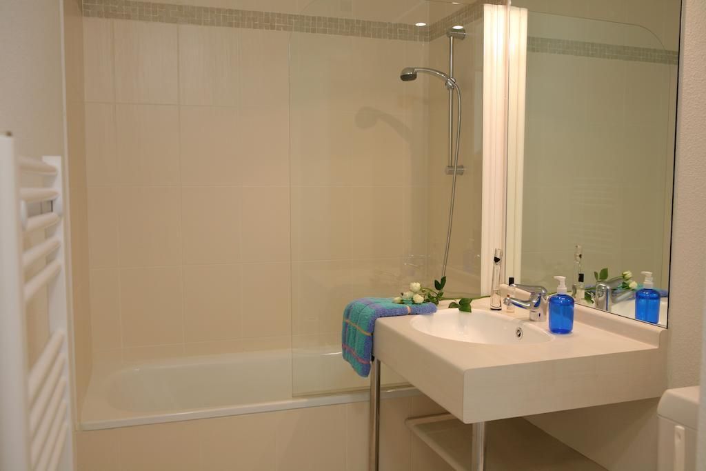 A bathroom with a glass-enclosed shower, a white sink with a mirror, and toiletries on the counter.