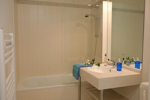 A bathroom with a glass-enclosed shower, a white sink with a mirror, and toiletries on the counter. - Residence Vacanceole Le Domaine de Bertheaume (Plougonvelin)