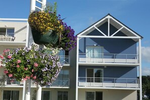 A multi-story building with balconies, a hanging flower basket, and a clear sky. - Residence Vacanceole Le Domaine de Bertheaume (Plougonvelin)