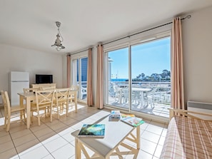 A room with a dining table, chairs, a TV, and a large window with curtains. - Residence Vacanceole Le Domaine de Bertheaume (Plougonvelin)