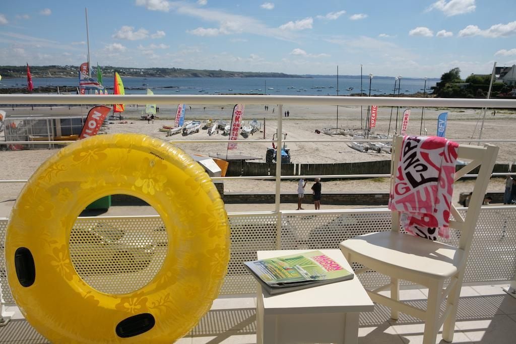A beach view from a balcony with a yellow inflatable ring, a magazine, and a chair with a towel.