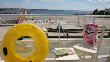 A beach view from a balcony with a yellow inflatable ring, a magazine, and a chair with a towel.