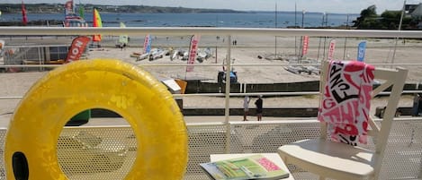 Vista al mar desde un balcón, con un flotador amarillo, una revista y una silla con una toalla.