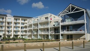 Ένα πολυώροφο ξενοδοχείο με μπαλκόνια, έναν τοίχο από πέτρα που λειτουργεί ως αναχωματισμός και έναν καθαρό ουρανό.