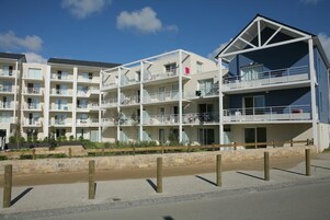 A multi-story hotel with balconies, a stone retaining wall, and a clear sky.