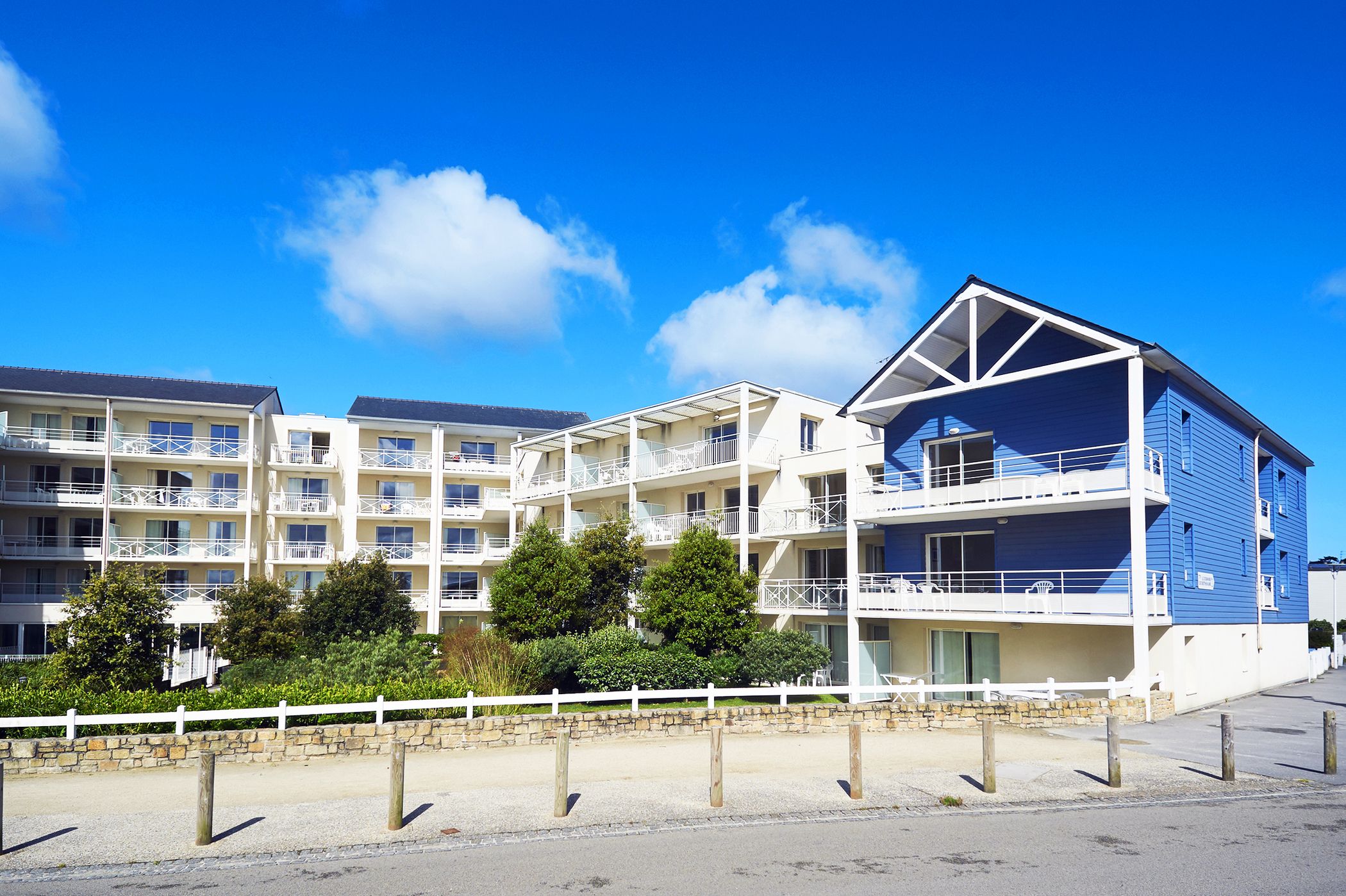 A multi-story hotel with balconies, a stone wall, and a white fence.