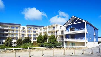 A multi-story hotel with balconies, a stone wall, and a white fence.