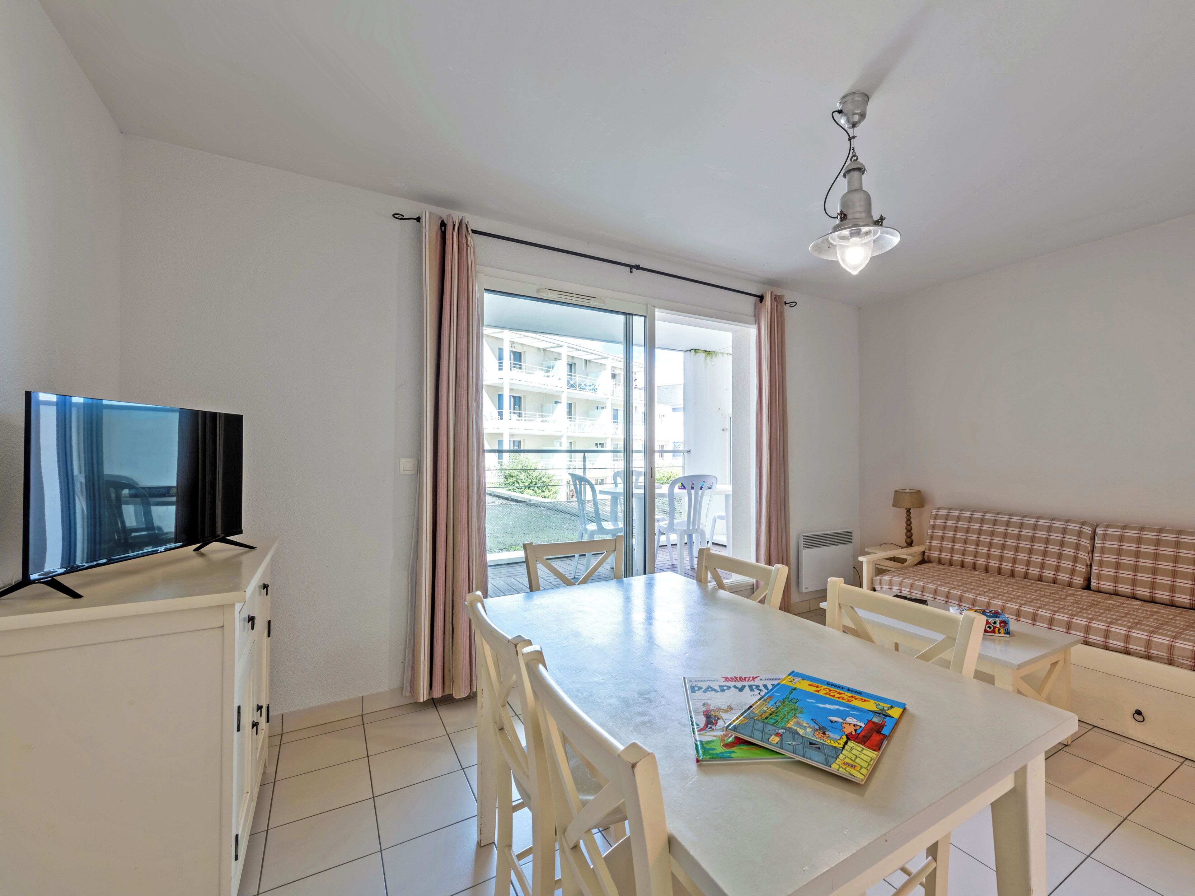 A room with a dining table, chairs, a sofa, a television, and a window with curtains.