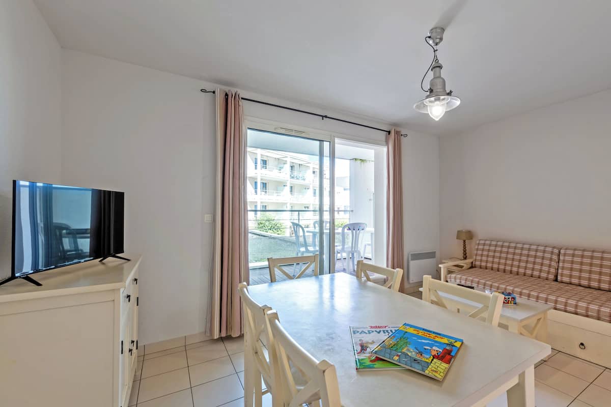 A room with a dining table, chairs, a sofa, a television, and a window with curtains.