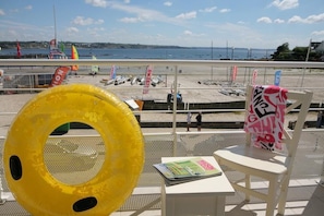 A beach view from a balcony with a yellow inflatable ring, a magazine, and a chair with a towel. - Residence Vacanceole Le Domaine de Bertheaume (Plougonvelin)