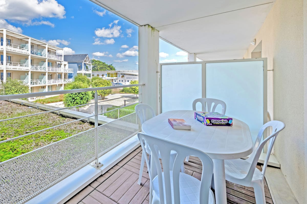 A balcony with a table and chairs, a view of buildings, and a clear sky.
