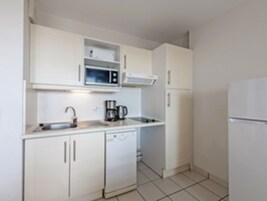 Una cocina compacta con armarios blancos, microondas, cafetera y refrigerador.