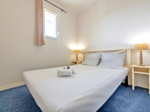 Et hotelværelse med en enkelt seng, et natbord med lampe og et vindue med gardiner.