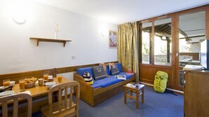 A cozy room with a wooden sofa, a small table with breakfast items, a chair, and a large window with curtains. - Les Hauts Du Rogoney (Val-d'Isere)