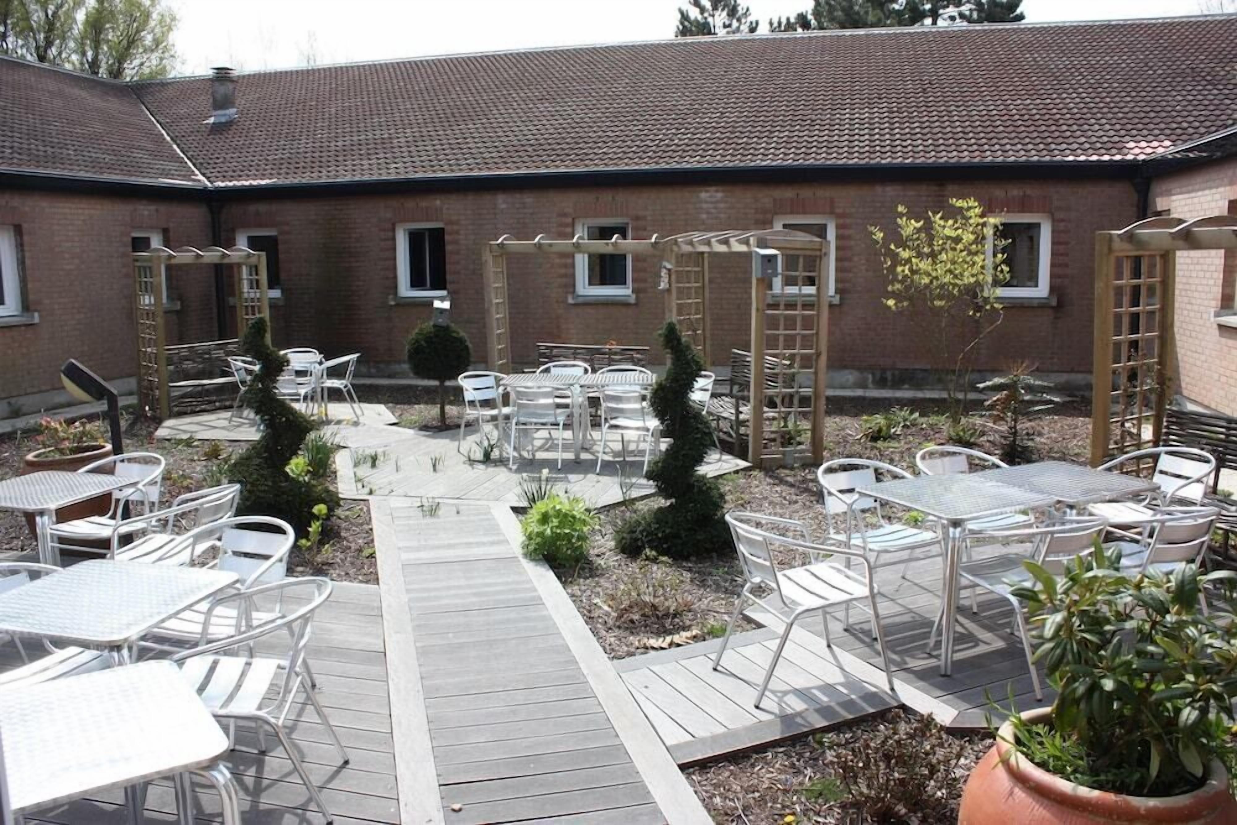 Un espace extérieur aménagé en terrasse, avec plusieurs tables et chaises, une plateforme en bois et un bâtiment en briques en arrière-plan.