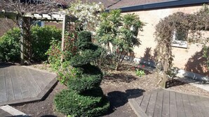 A garden area with a wooden pergola, various shrubs, and a brick building in the background. - Brit Hotel Essentiel Dunkerque Gravelines (Gravelines)