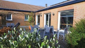 A brick building with a tiled roof, a patio with chairs and a table, and a window with a view. - Brit Hotel Essentiel Dunkerque Gravelines (Gravelines)