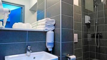 Une salle de bain moderne avec des carreaux foncés, un lavabo blanc, des toilettes et une douche séparée par une paroi de verre.