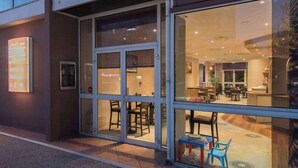 A modern hotel entrance with glass doors, a reception desk inside, and a seating area with tables and chairs. - Brit Hotel Tours Sud Le Cheops (Joue-les-Tours)