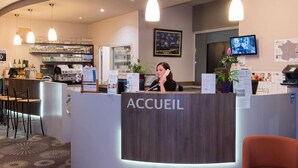 A reception area with a counter labeled "ACCUEIL," a bar area with stools, and a television mounted on the wall. - Brit Hotel Tours Sud Le Cheops (Joue-les-Tours)