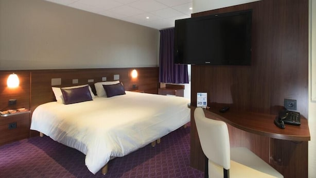 A hotel room with a large bed, a desk with a chair, a flat-screen TV mounted on the wall, and a nightstand with a lamp. - Brit Hotel Tours Sud Le Cheops (Joue-les-Tours)