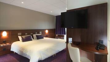 Habitación de hotel con una cama grande, un escritorio con silla, un televisor de pantalla plana en la pared y una mesita de noche con lámpara.