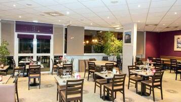 Un restaurante con varias mesas y sillas, amplios ventanales y plantas de interior.